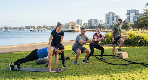 A small team of Geelong corporate workplace colleagues doing low-impact team circuit training together with a trainer in natural morning daylight.
