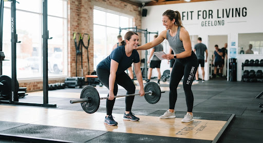 A smiling female trainer coaching an adult client during their first session on a clean timber lifting platform at Fit For Living Geelong, bright natural daylight, calm focused atmosphere.